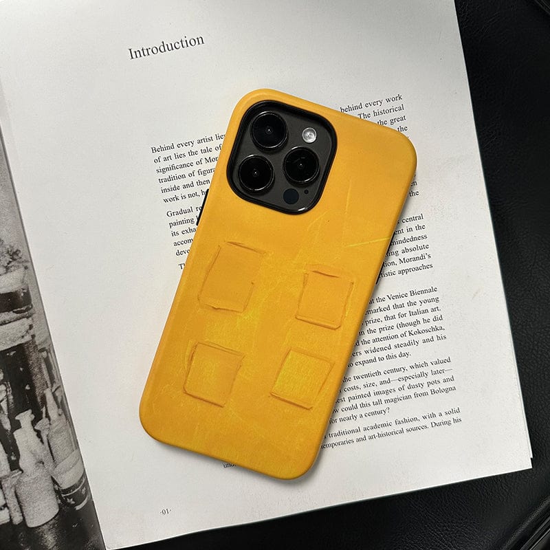 A smartphone with a Bold Yellow Textured iPhone 16 Pro Max case is placed on top of an open book. The case, featuring a unique modern art design with multiple rectangular indentations, leaves the phone's camera lenses visible. The page of the book displays text under the heading "Introduction.