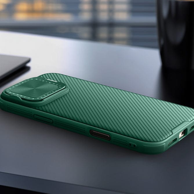 A Shockproof Slim Fit iPhone 16 Pro Max Case with MagSafe, dual-layer protection, and a camera cover, featuring a textured, ergonomic anti-slip grip in green is shown on a table next to a laptop and a coffee mug.