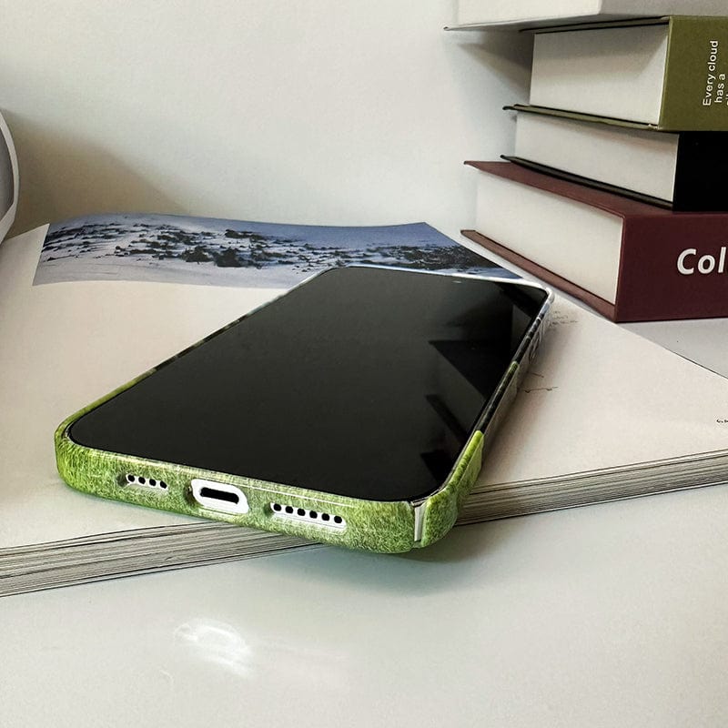 A smartphone in a Mountain Landscape iPhone 16 Pro Max case, featuring an "All or Nothing" quote, rests facedown on an open book with a photograph of snow-covered mountains. Nearby, there are three stacked closed books. The image conveys a cozy, relaxed setting.