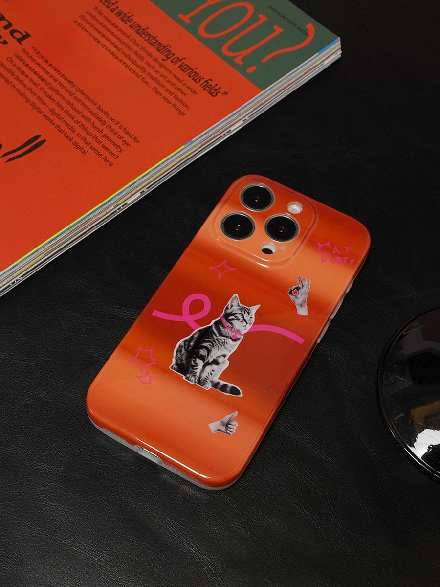 An iPhone 16 Pro Max, encased in a Cat Vibes iPhone 16 Pro Max Case featuring a playful orange gradient design adorned with stickers of a cat, pink squiggles, and a thumbs-up hand, rests on a black surface next to an open, colorful magazine.