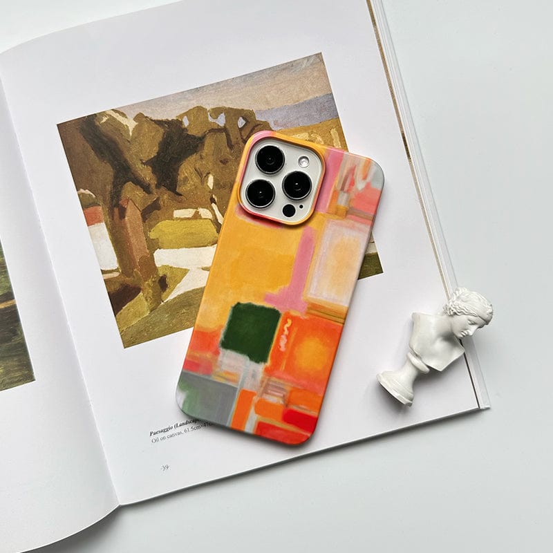 A smartphone equipped with a Modern Abstract Color Block iPhone 16 Pro Max Case - Vibrant Artistic Design with Full Protection is placed on an open art book featuring a landscape painting. A small white classical bust sculpture is positioned next to the smartphone, all set on a light-colored surface.