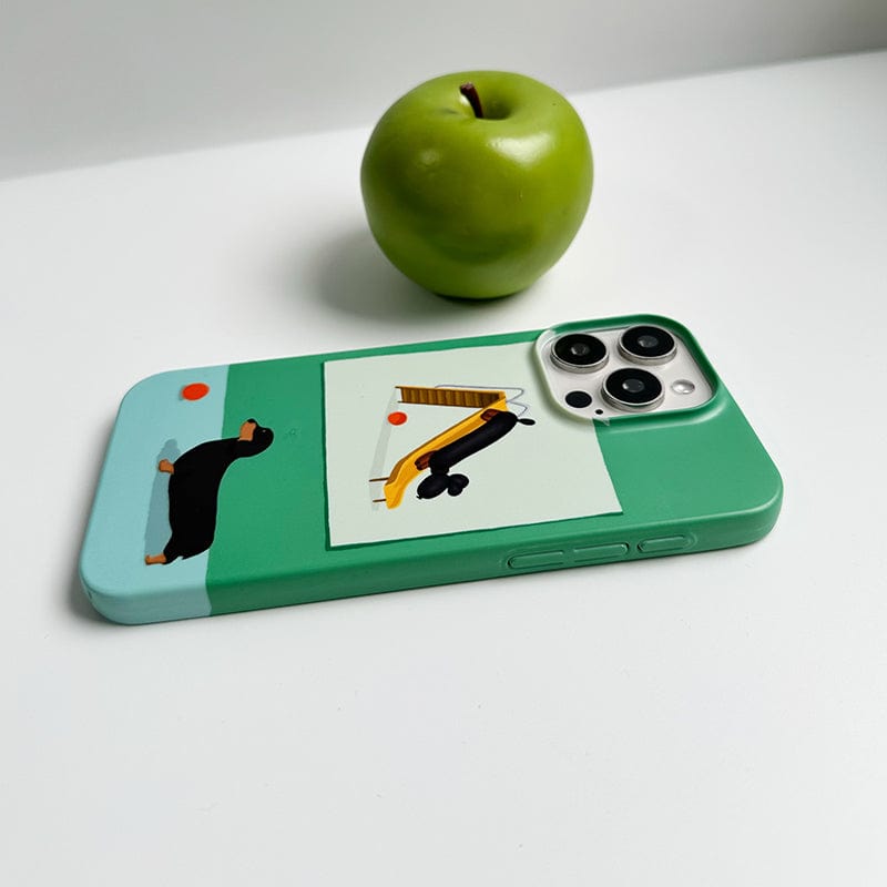 A green smartphone with a Playful Dachshund iPhone 16 Pro Max case, showcasing a cute green and blue design, lies on a white surface. A green apple is placed upright in the background.