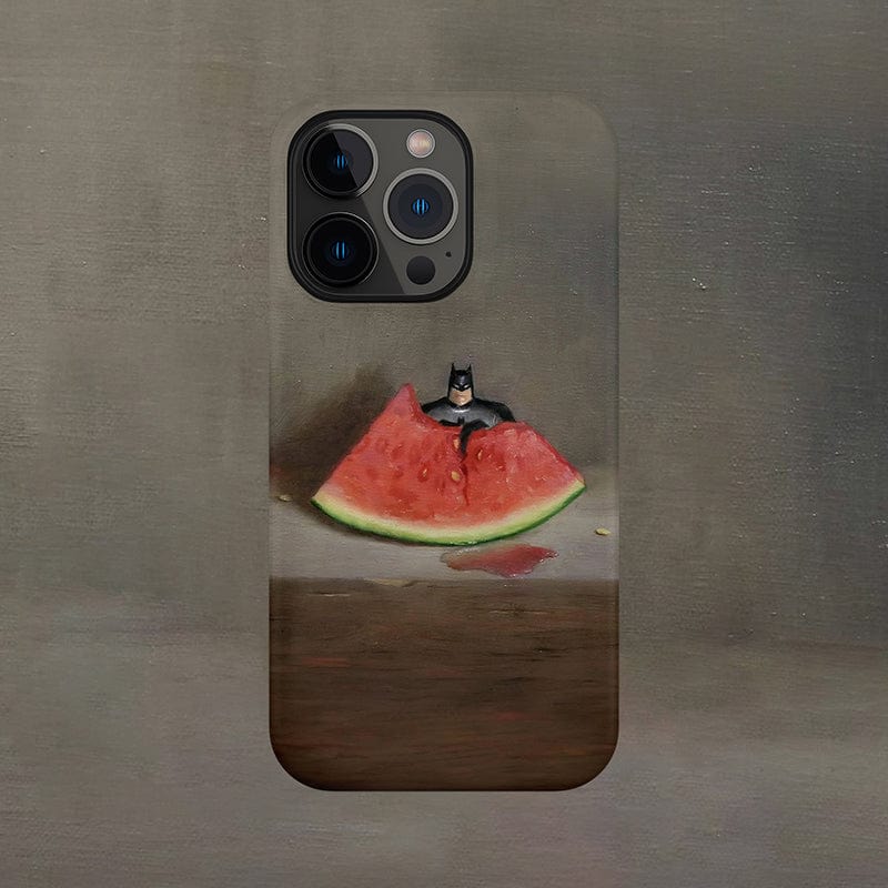 The Quirky Watermelon & Miniature Hero iPhone 16 Pro Max Case showcases a painted watermelon slice against a muted background, with a small Batman figurine perched atop the fruit, creating a whimsical and unexpected contrast between the everyday fruit and the iconic superhero.