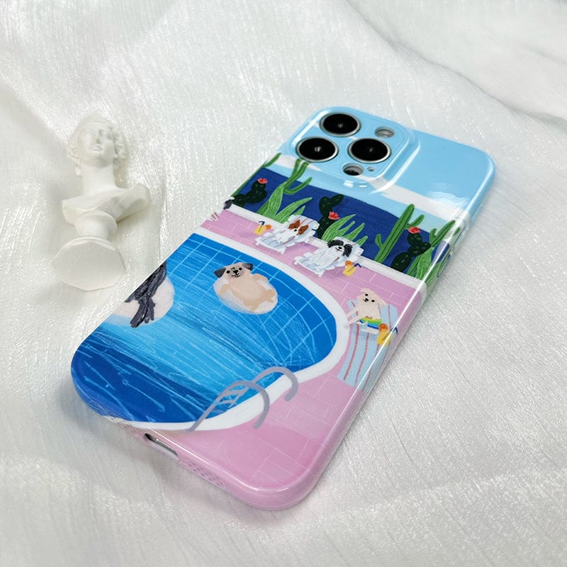 A smartphone displays the "iPhone 16 Pro Max Case with Relaxing Poolside Dogs - Cute and Protective," featuring an illustration of a pool scene. The pool water is blue, with several cute dogs around it—one is lounging on a float in the pool. The background includes cacti and birds perched on a fence, while a small bust sculpture rests beside the phone on a white fabric surface.