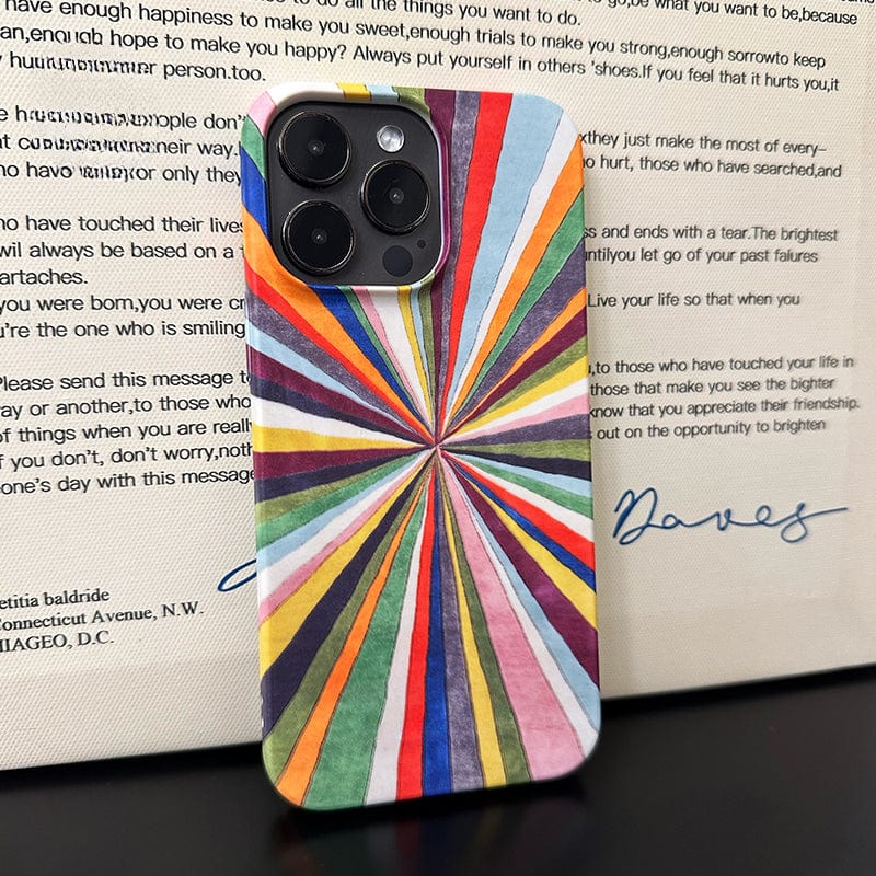 A Vibrant Burst iPhone 16 Pro Max Case, featuring a colorful radiant stripes design with full protection, is placed in front of an open book. The case showcases vibrant rays extending outward from a central point, creating a vivid starburst effect. The book has cursive handwriting on its pages.