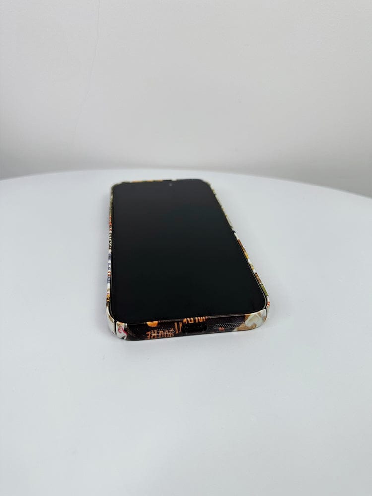 A smartphone adorned with the Retro Collage iPhone 16 Pro Max Case - Artistic and Protective is lying flat on a white surface, its screen turned off and displaying a black screen.