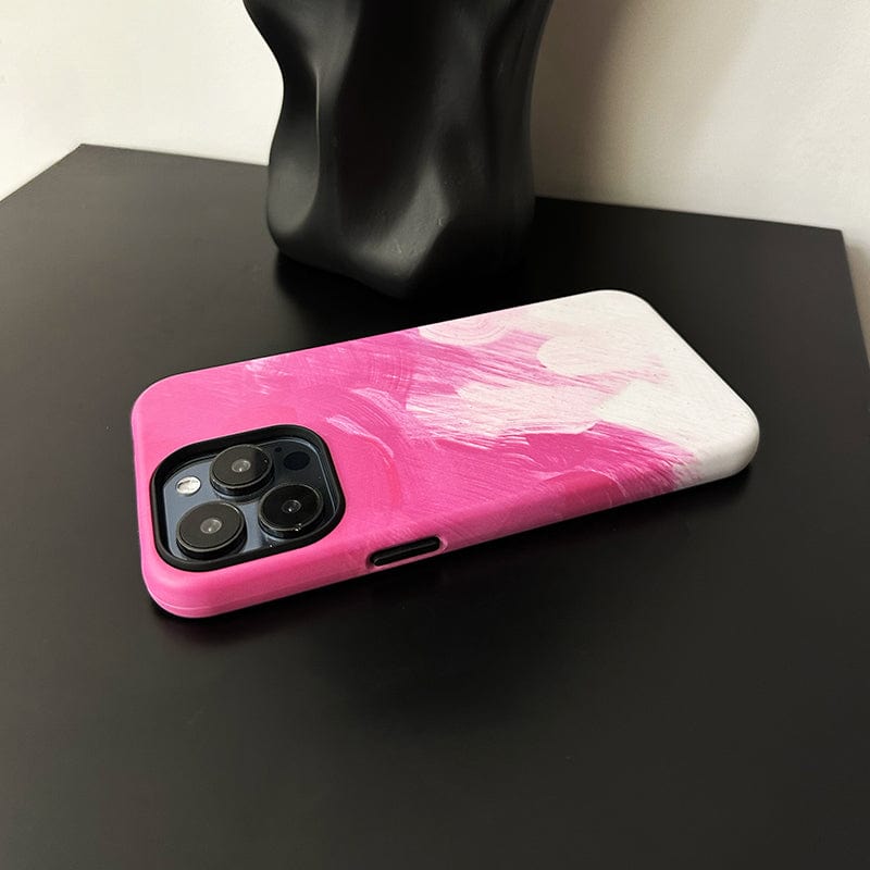 An iPhone 16 Pro Max in a Bold Pink Brushstroke case with an artistic design and full protection is placed face-down on a black surface. A black abstract object is visible in the background, and the phone's camera lenses are partially visible.