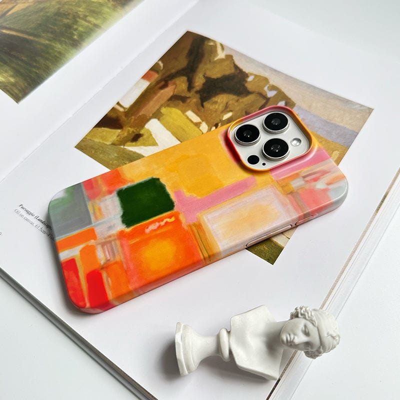 A smartphone fitted with a Modern Abstract Color Block iPhone 16 Pro Max Case - Vibrant Artistic Design with Full Protection is placed on an open art book showcasing a painting. Beside the phone is a small, white bust sculpture. The scene appears on a white surface, creating a minimalistic and artistic setup.