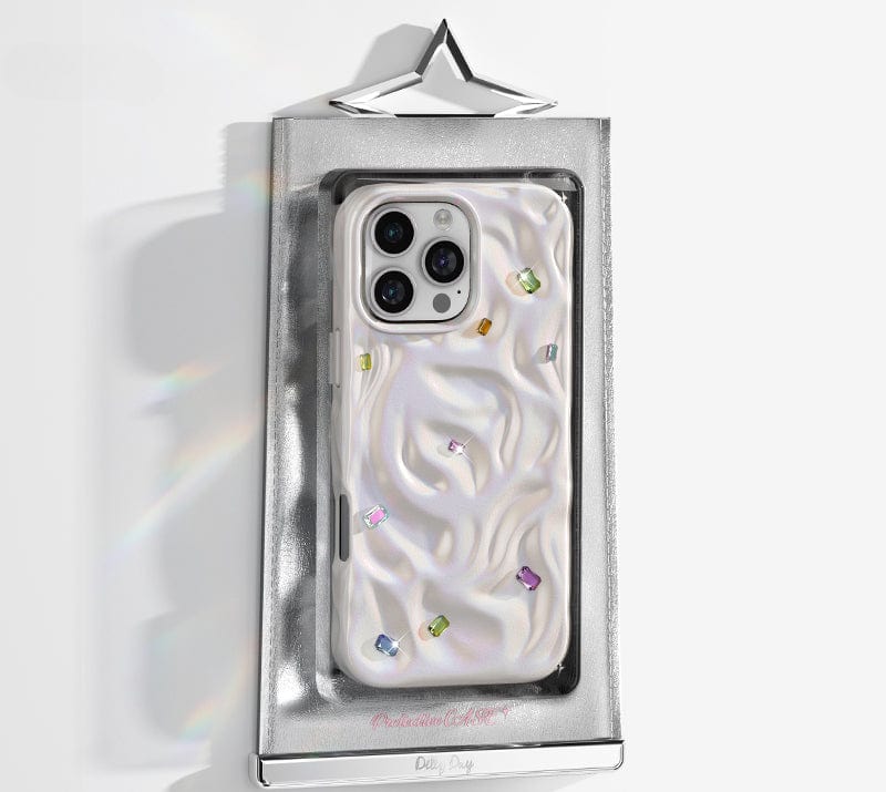 A luxurious iPhone 16 Pro Max case, featuring a glossy, wavy-textured design with handcrafted gemstone details, is showcased in its shiny silver packaging against a white backdrop.