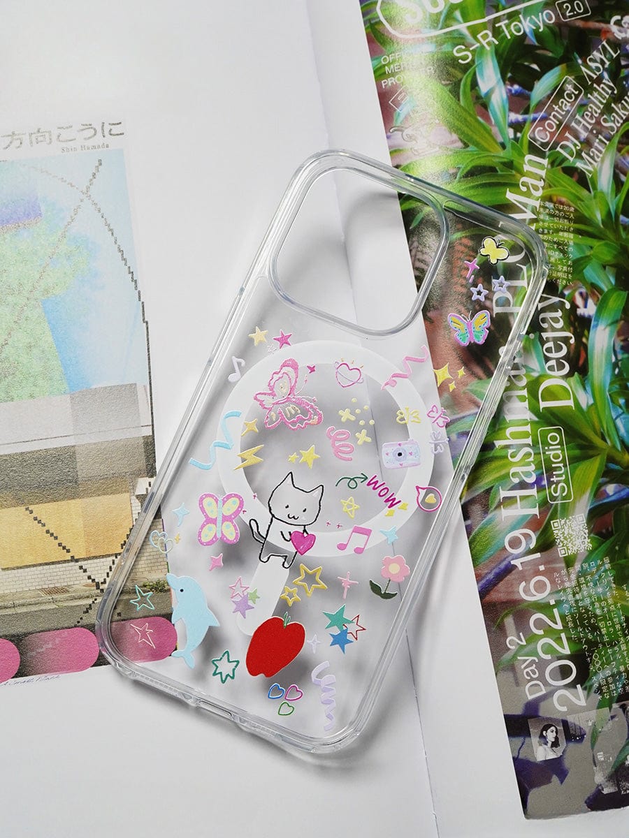 The Whimsical Dreams MagSafe iPhone 16 Pro Max Case, a transparent and playful all-inclusive protective cover decorated with colorful stickers featuring a cat, hearts, stars, flowers, and musical notes, is lying on printed paper adorned with geometric and text elements.