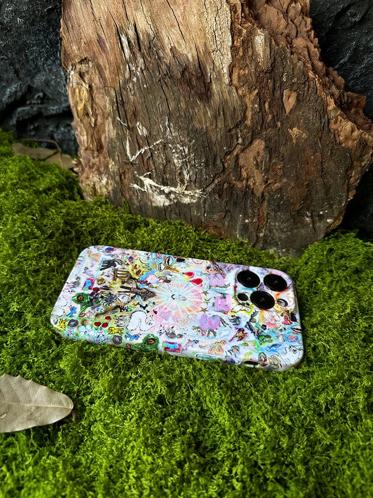 A smartphone outfitted with the Whimsical Dreamscape iPhone 16 Pro Max Case, featuring a fantasy-inspired artistic design, is placed on a bed of green moss. The phone's three camera lenses are visible in the top left corner. In the background, there is a piece of wood and some dried leaves.