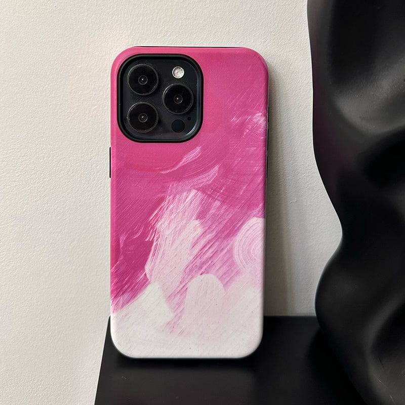 A Bold Pink Brushstroke iPhone 16 Pro Max Case - Artistic Design with Full Protection rests against a white wall, positioned next to a black sculptural object, partially visible on the right side of the image.