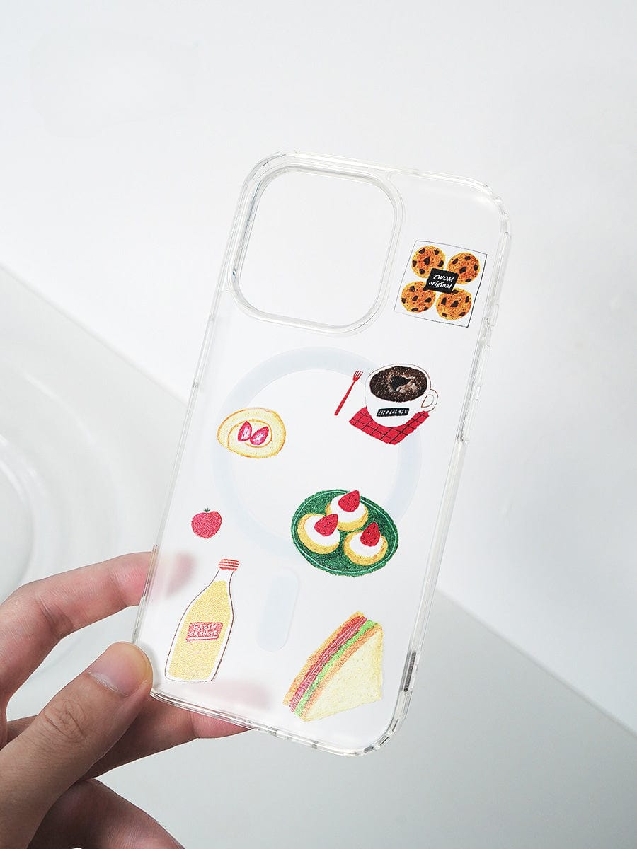 A hand holds the Brunch Time MagSafe iPhone 16 Pro Max Case, which showcases an adorable 3D food design. The transparent case is decorated with a sandwich, a bowl of ramen, a plate with eggs and sausage, cookies, a bottle of milk, and a cup of coffee. The empty phone camera slot remains visible.