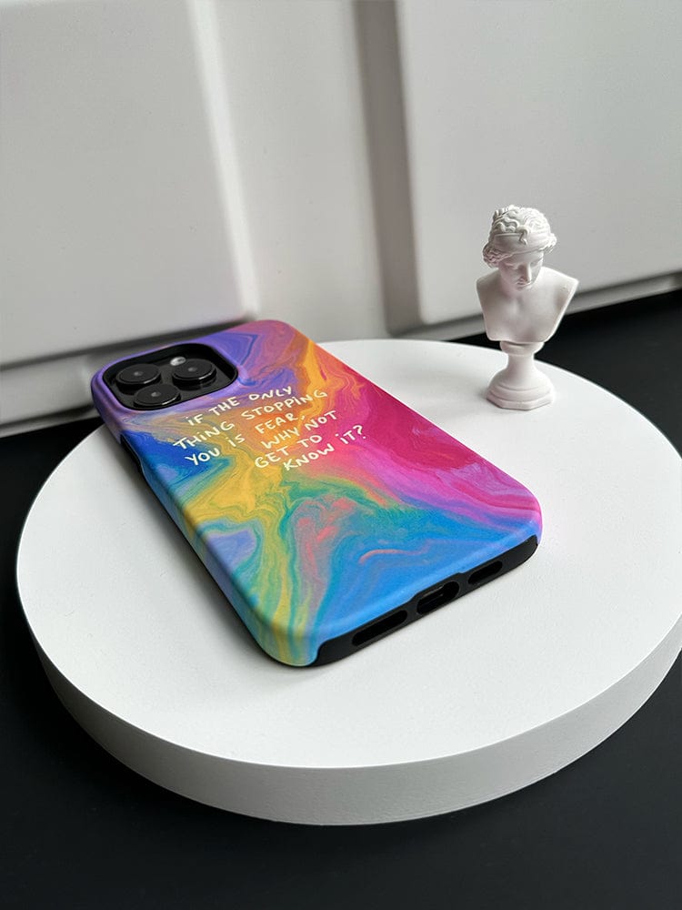 An iPhone 16 Pro Max, encased in the Inspirational Swirl iPhone 16 Pro Max Case with a colorful abstract design and a motivational quote reading, "If the only thing you steal is my time, isn’t it only fair I get to kill yours?" sits on a white circular platform. A small white bust sculpture is placed next to the phone.