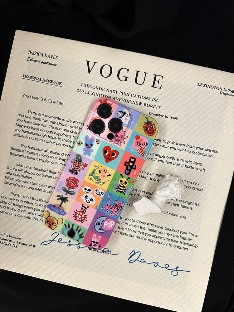 A Colorful Kawaii Patchwork iPhone 16 Pro Max Case, known for its cute and vibrant design with full protection, rests on a Vogue magazine cover. The phone case, adorned with whimsical character illustrations, partially obscures the magazine text. Next to the phone on the magazine lies a white lace item.