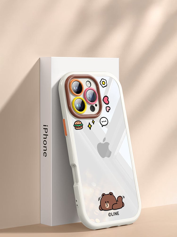 An iPhone 16 Pro Max, adorned with a cute cartoon clear protective cover featuring a bear and various small icons, is propped against its packaging, showcasing its shockproof bumper and anti-scratch lens protection.