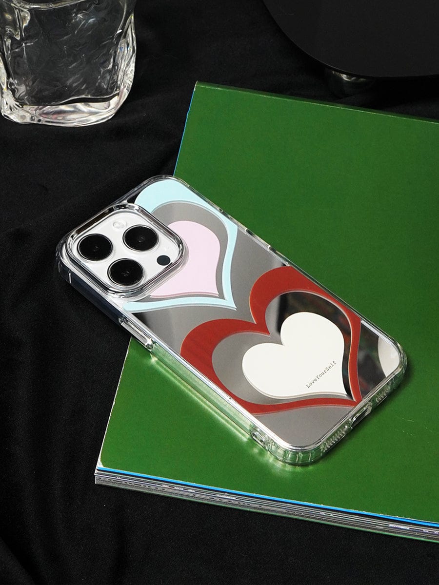 An iPhone 16 Pro Max with a Retro Heart Layers Case featuring a vibrant Love Yourself design rests on a closed green notebook.