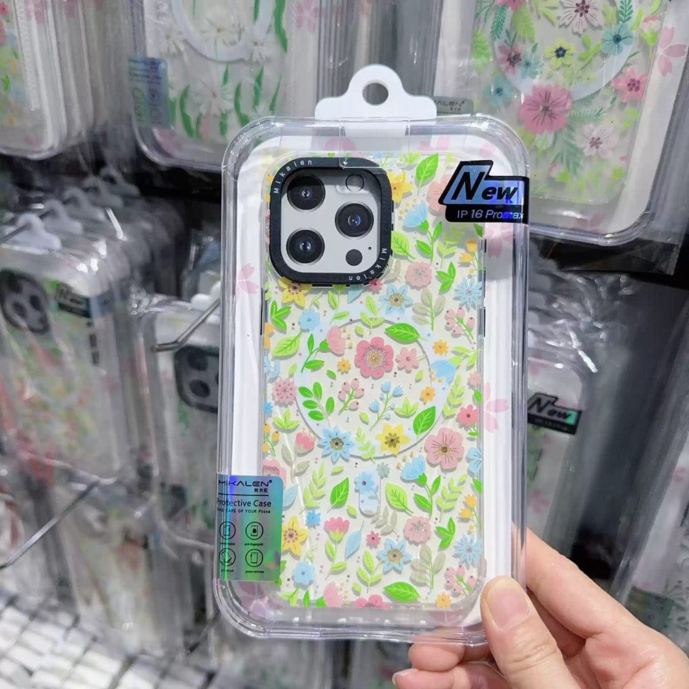 A person holds a packaged Floral MagSafe iPhone 16 Pro Max Case featuring a vibrant 3D flower design and shockproof clear cover, displayed among other similar cases in a store.